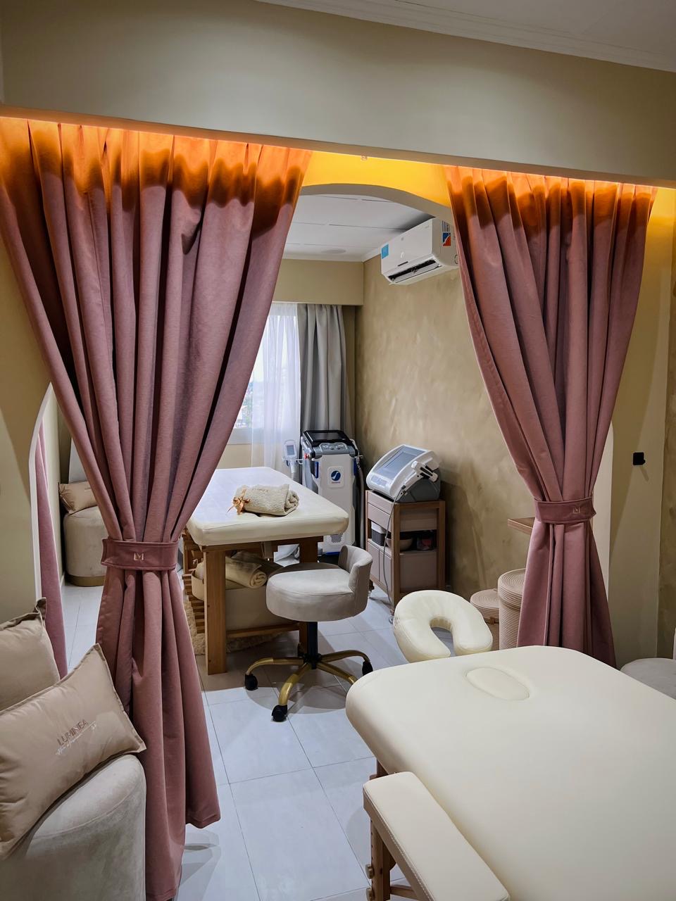 Sala de tratamientos de LUMINEA ESTETICA con camillas y cortinas cálidas